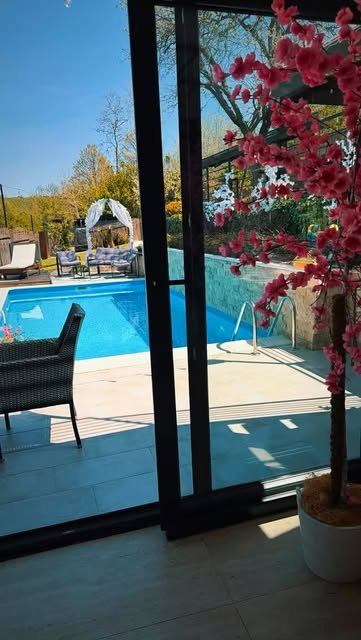 Pogled na bazen Green Garden u Barajevu kroz staklena vrata, sa buganvilijom i ležaljkama